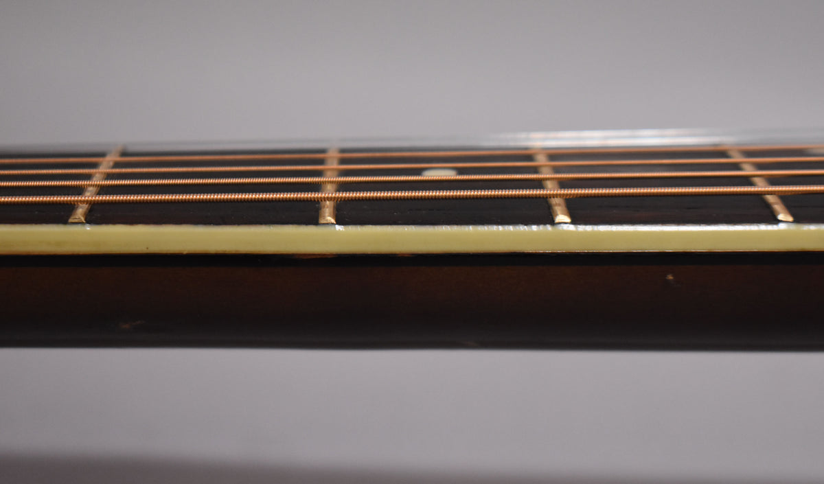 Close-up of the guitar's dark fretboard and light binding, showing copper strings, metal frets, and a single white fret marker.