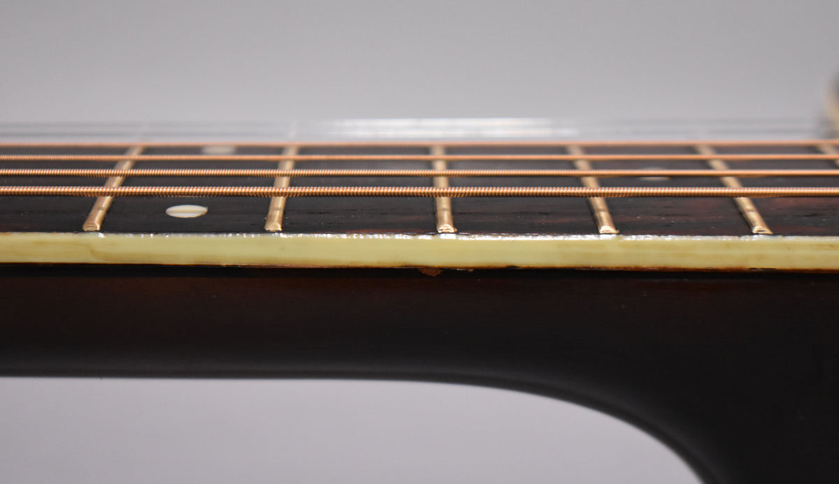 Close-up of the guitar's dark fretboard and neck, showing light-colored binding, copper strings, and a small chip in the binding.