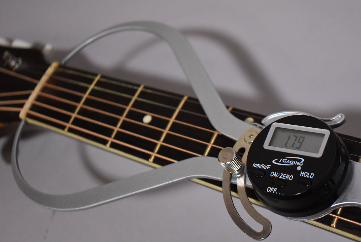 A digital caliper measures the nut width of the dark fretboard, showing "1.79" on its display.