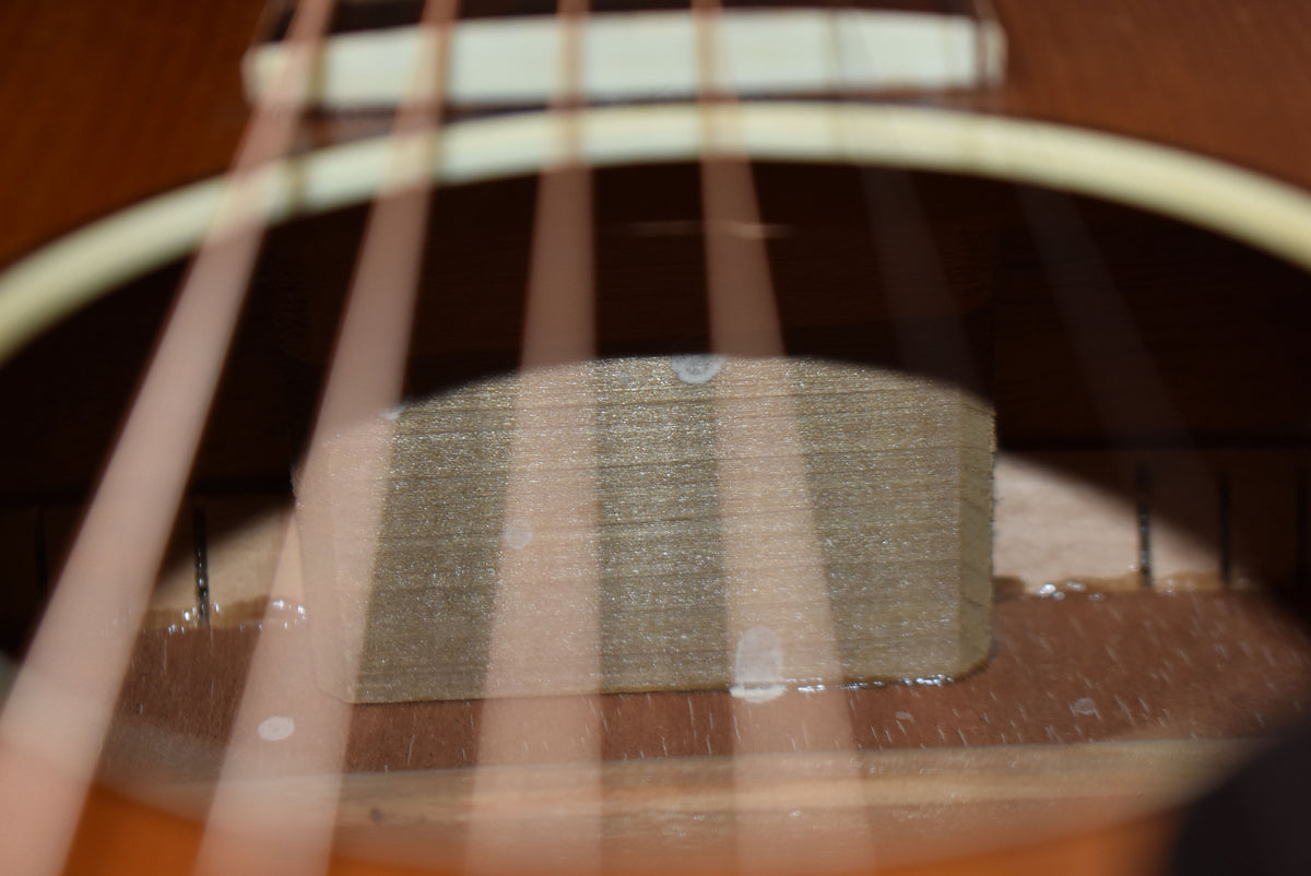 Close-up inside the soundhole shows the light-colored internal bracing and a rectangular label, with visible glue residue.