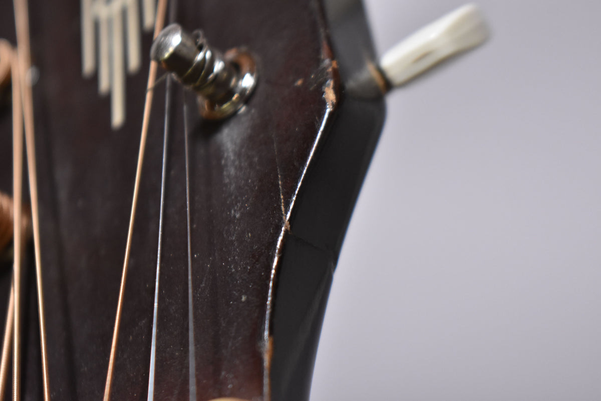 Close-up of the dark brown headstock, showing a chrome tuner, strings, and significant finish checking and wear along the edge.