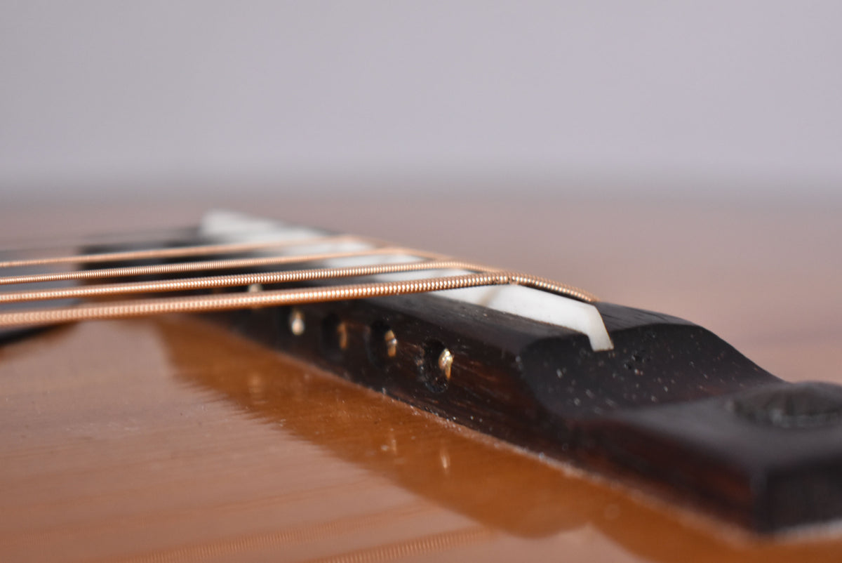 Close-up of the guitar's dark bridge and white saddle, with six bronze strings running over it, against a glossy sunburst body.
