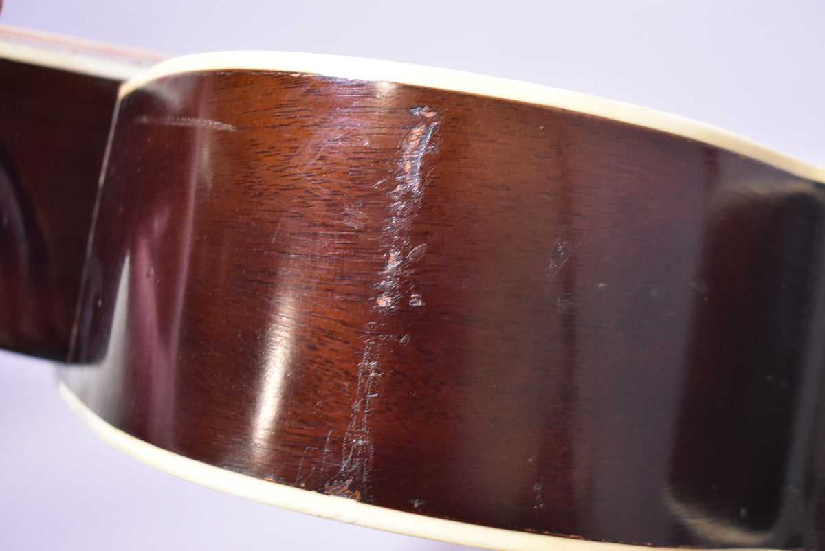 Close-up of the guitar's dark brown side, showing significant finish wear, scratches, and chips along the binding.