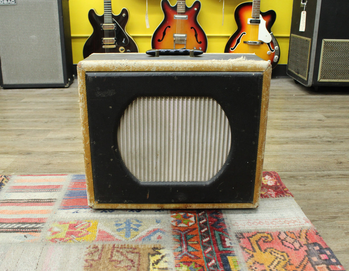 Front view of a tweed and black combo amp with a round speaker grille, showing wear and frayed edges.