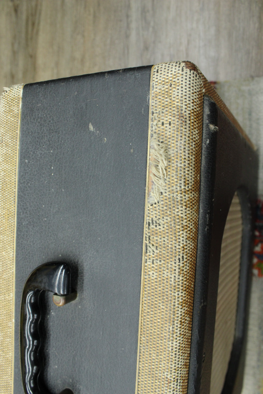 Close-up of the amp's top left corner, showing a black handle, worn black tolex, and frayed tweed grille cloth.