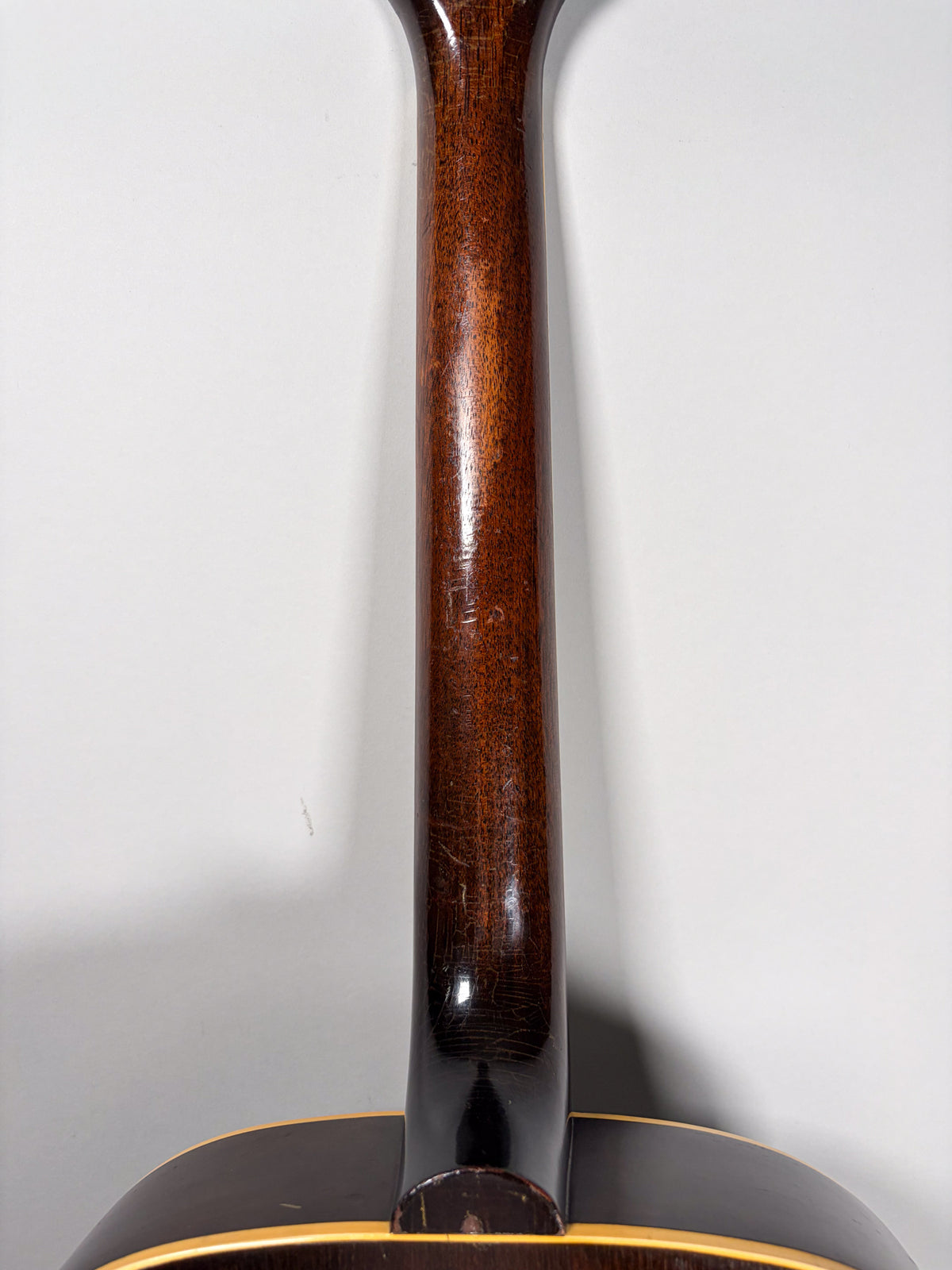The guitar's dark brown neck, seen from behind, shows extensive finish checking and wear, especially near the heel and headstock.