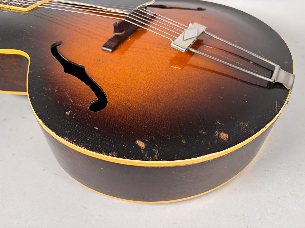 Close-up of the sunburst archtop guitar's lower bout, showing the f-hole, trapeze tailpiece, and heavy finish wear and checking on the dark edges.