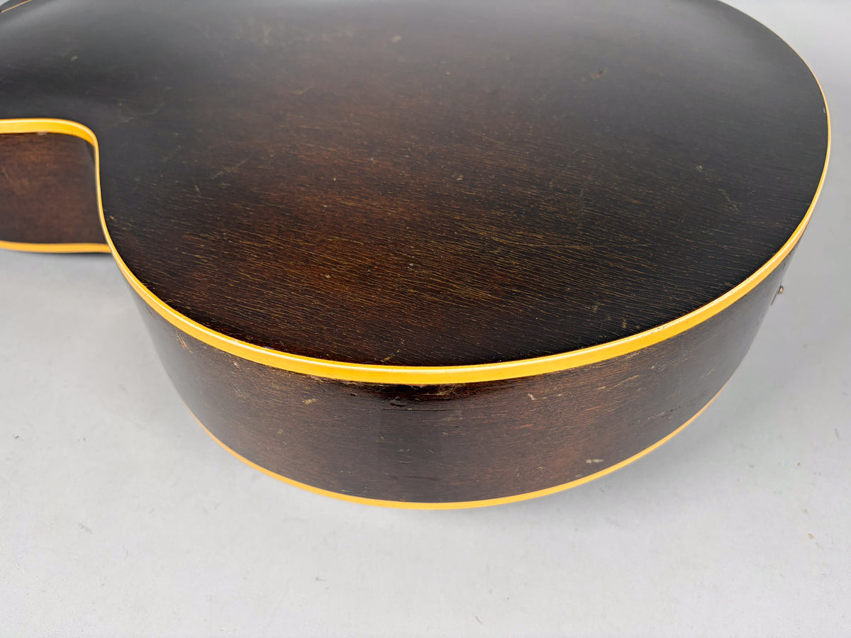 The guitar's dark brown back and side are visible from the upper bout, showing yellow binding and extensive finish wear and checking.