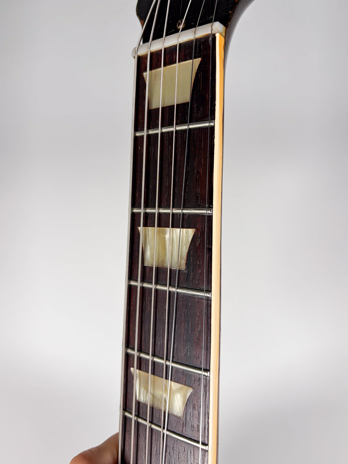 Close-up of the dark rosewood fretboard with trapezoid mother-of-pearl inlays, showing some wear and light checking on the binding.