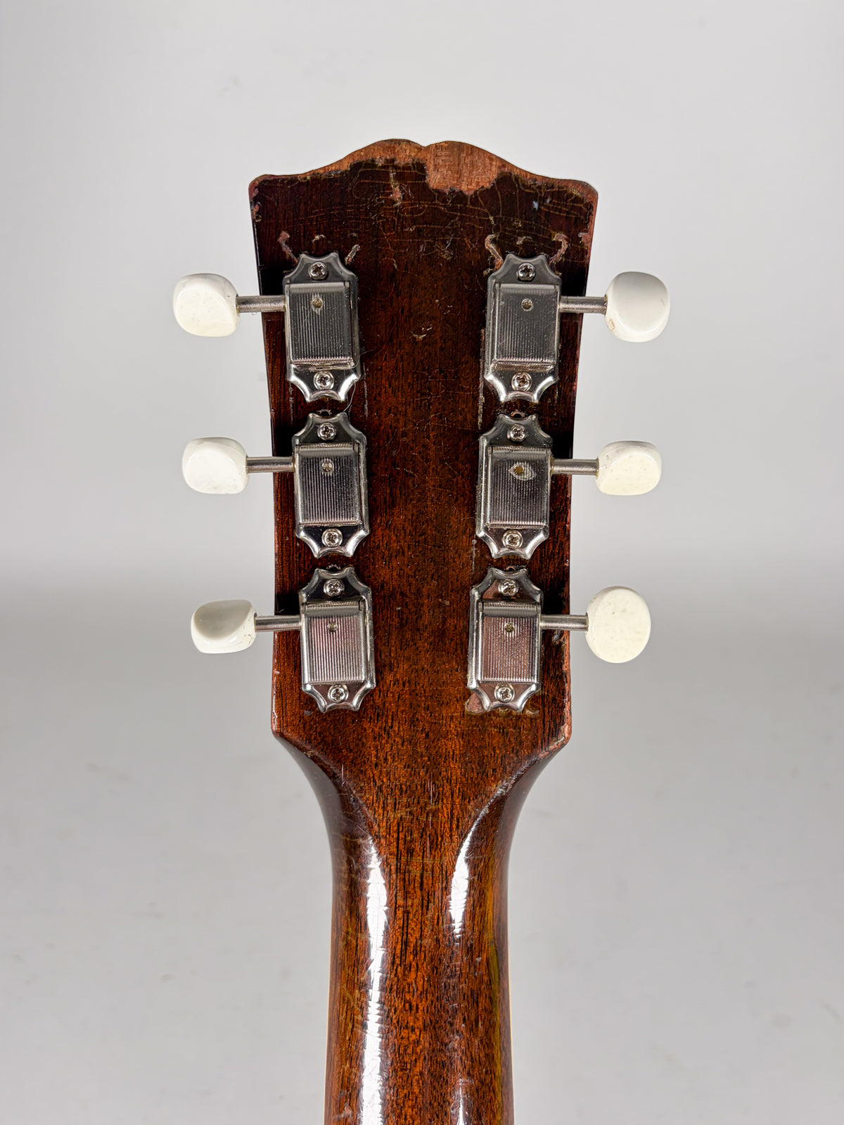 The back of a dark brown guitar headstock with six white tuning pegs and chrome tuners, showing significant finish wear.