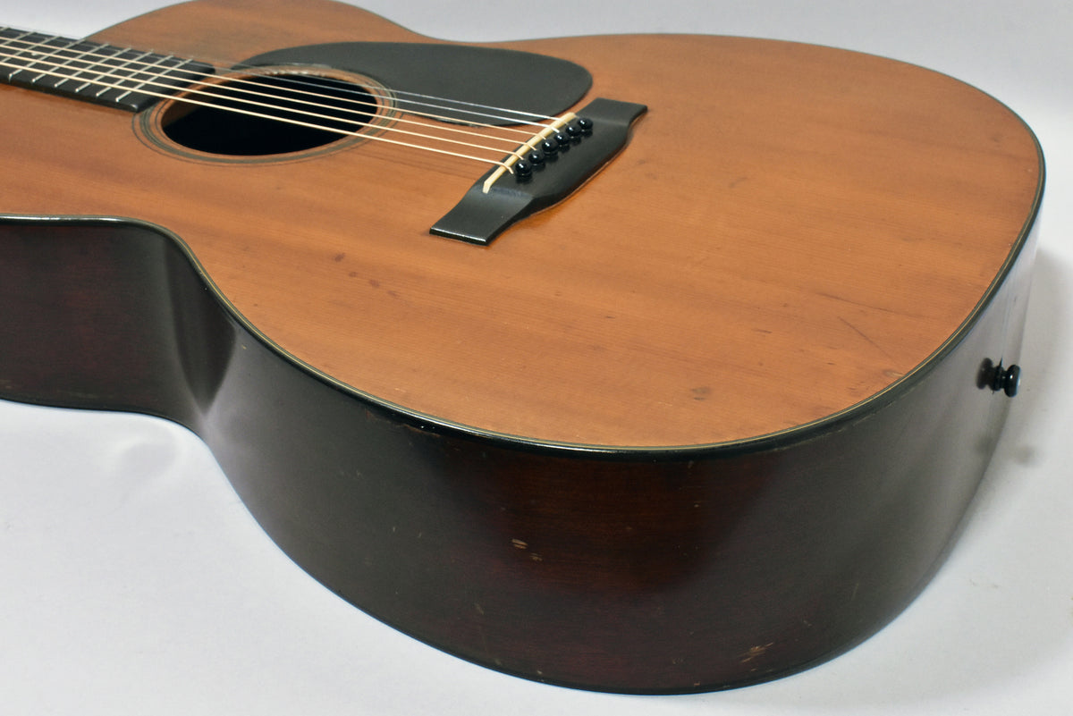 Close-up of the guitar's lower bout, showing the natural finish top, dark sides, black pickguard, bridge, and strap button.