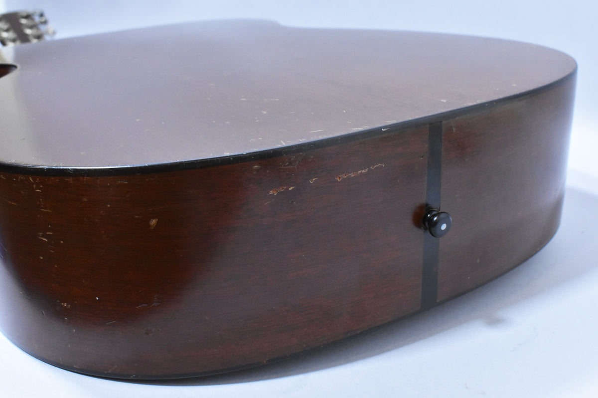 The guitar's dark brown side and back show heavy wear, scratches, and finish checking, with a black endpin jack.