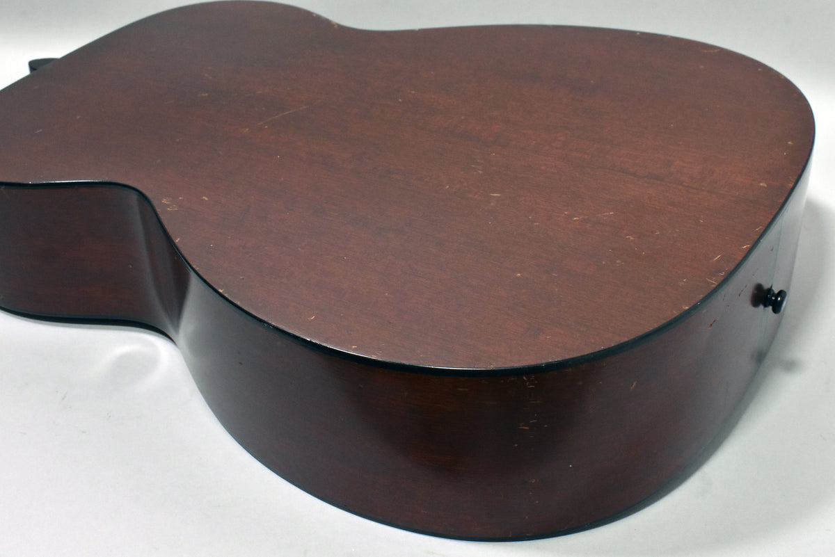 The guitar's dark brown back and side are visible from an angle, showing light scratches, wear, and a black strap button.