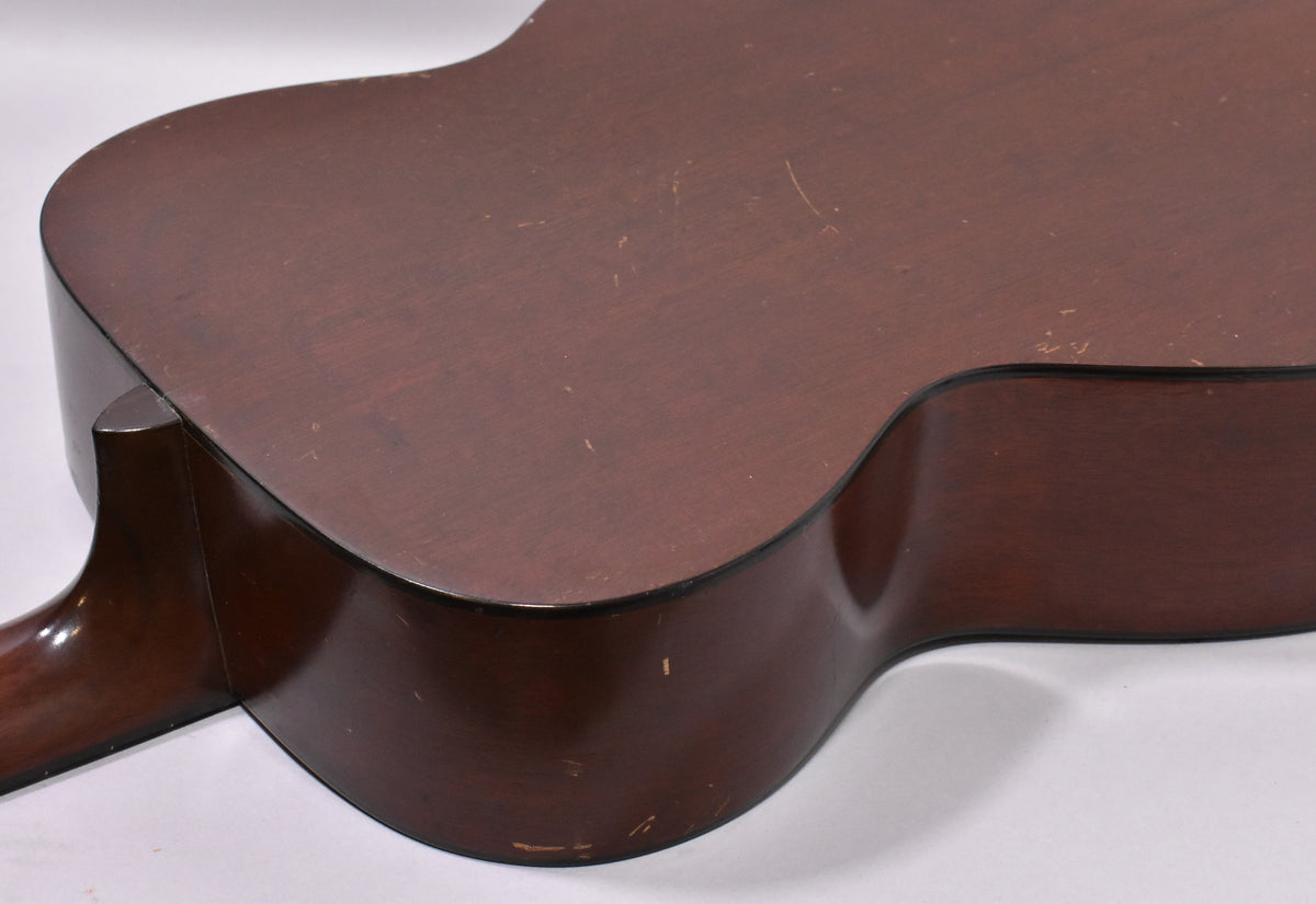The lower bout and waist of the dark brown acoustic guitar, showing a matte finish with many scratches and dings.