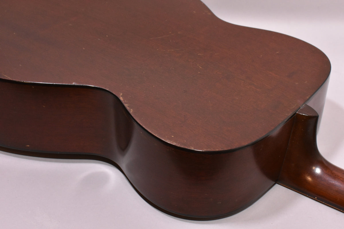 The guitar's dark brown back and side are visible from the lower bout, showing light scratches and edge wear on the natural finish.