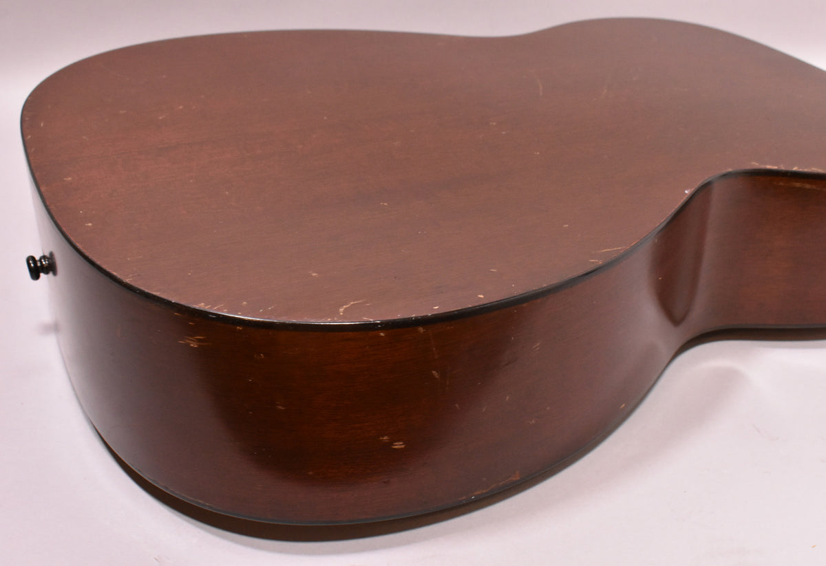 The lower bout of a dark brown acoustic guitar, showing a matte finish with visible wear, scratches, and a black endpin.