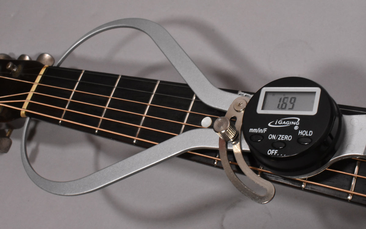A digital caliper measures the nut width of the dark fretboard, displaying "1.69" on its screen.