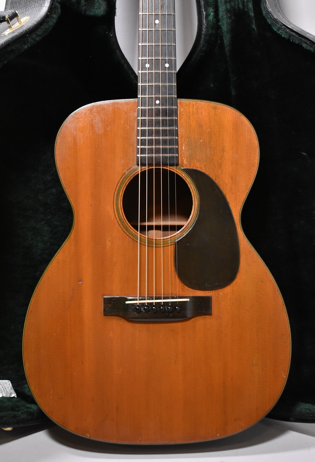 Full front view of a natural finish acoustic guitar with a dark pickguard, showing visible wear and checking on the body.