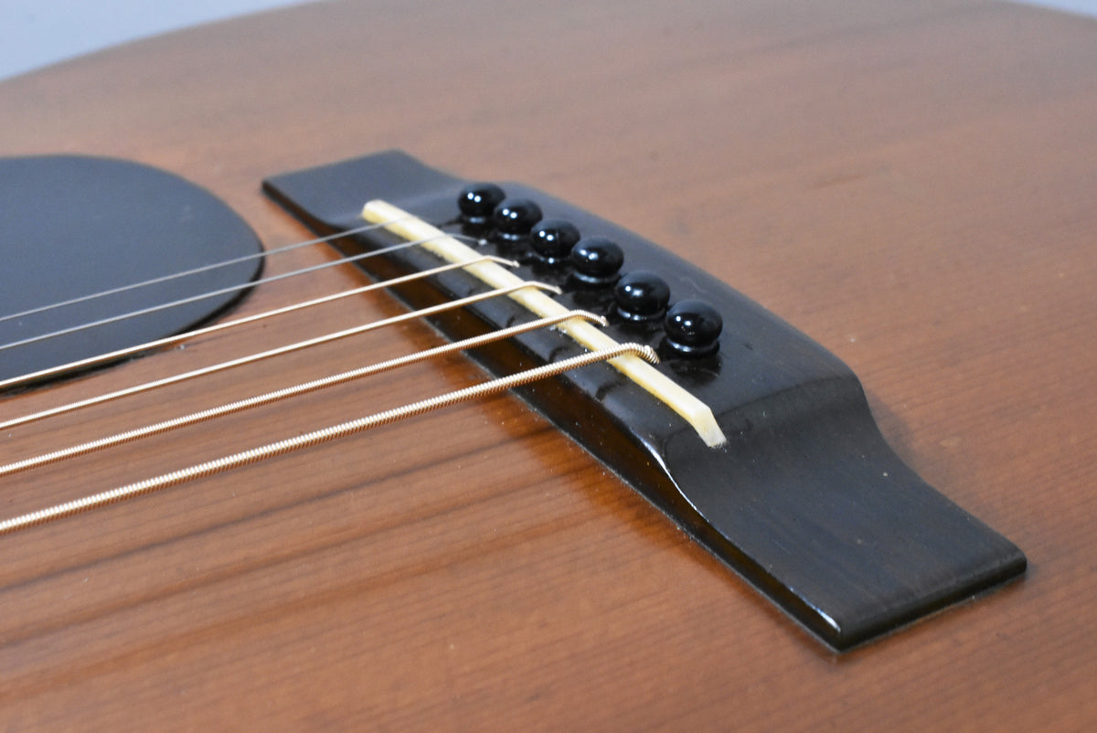 Close-up of the guitar's dark bridge with six black pins and a light saddle, showing light wear on the natural wood body.