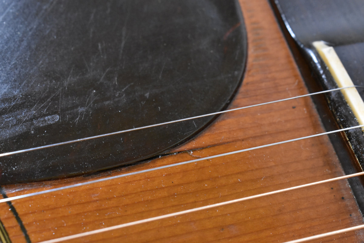 Close-up of the guitar's lower bout, showing the worn black pickguard, natural wood finish, and a crack near the bridge.