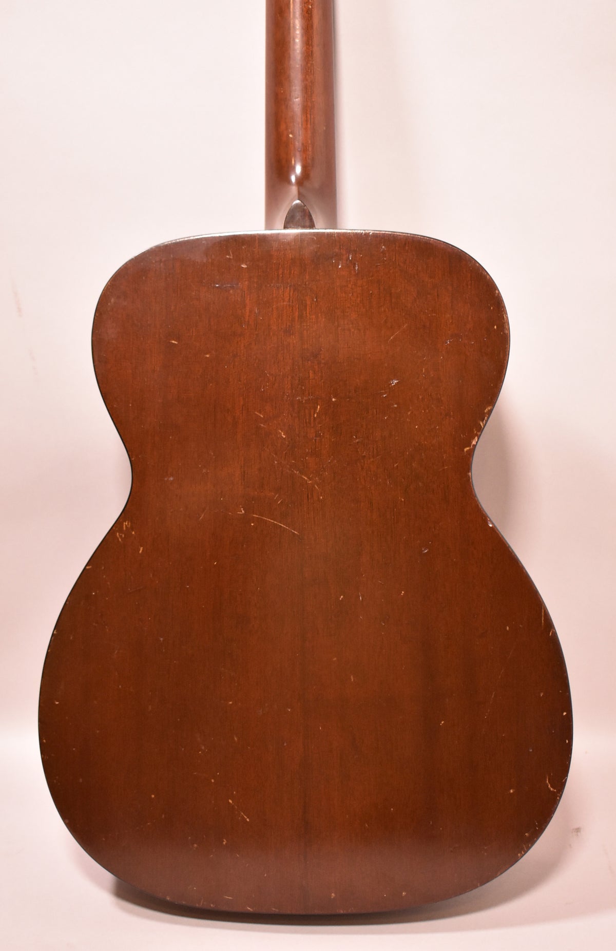 Full back view of the dark brown acoustic guitar, showing many light scratches and scuffs across the satin finish.