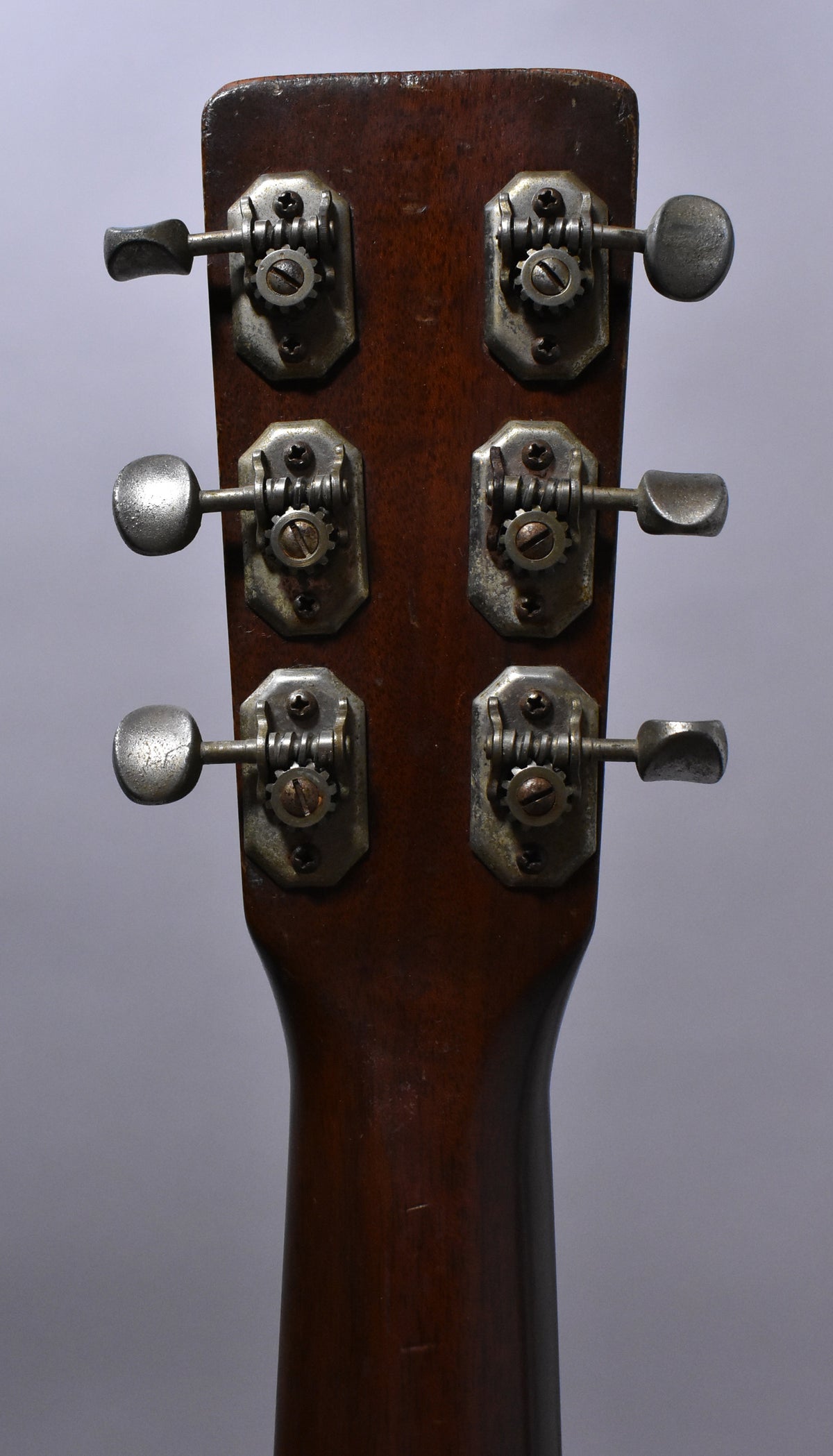 The back of the guitar's headstock and upper neck, showing six tarnished open-gear tuners with metal buttons on a dark brown finish.