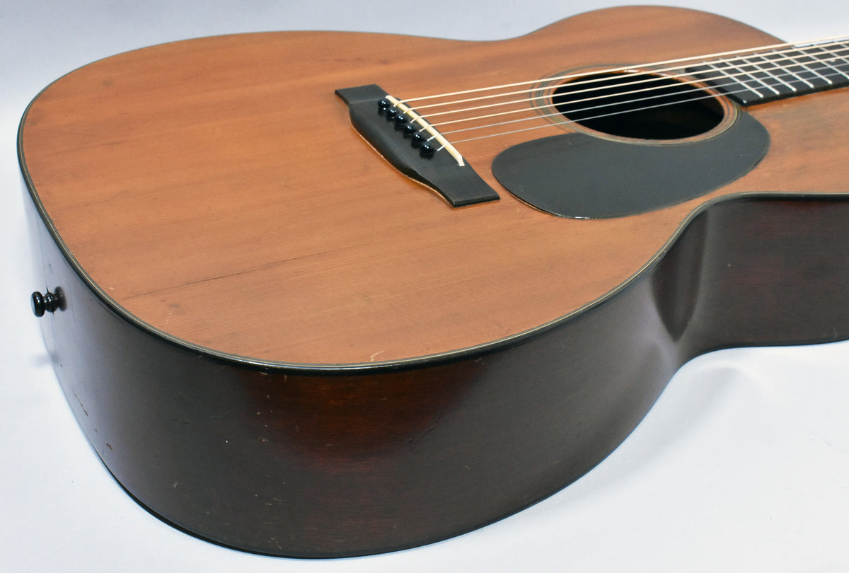 The acoustic guitar's natural finish top and dark sides show wear, with a black pickguard and bridge visible.
