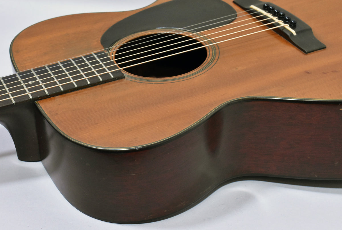 The upper bout of the acoustic guitar, showing the natural finish top, dark pickguard, dark sides, and some finish wear on the lower bout.
