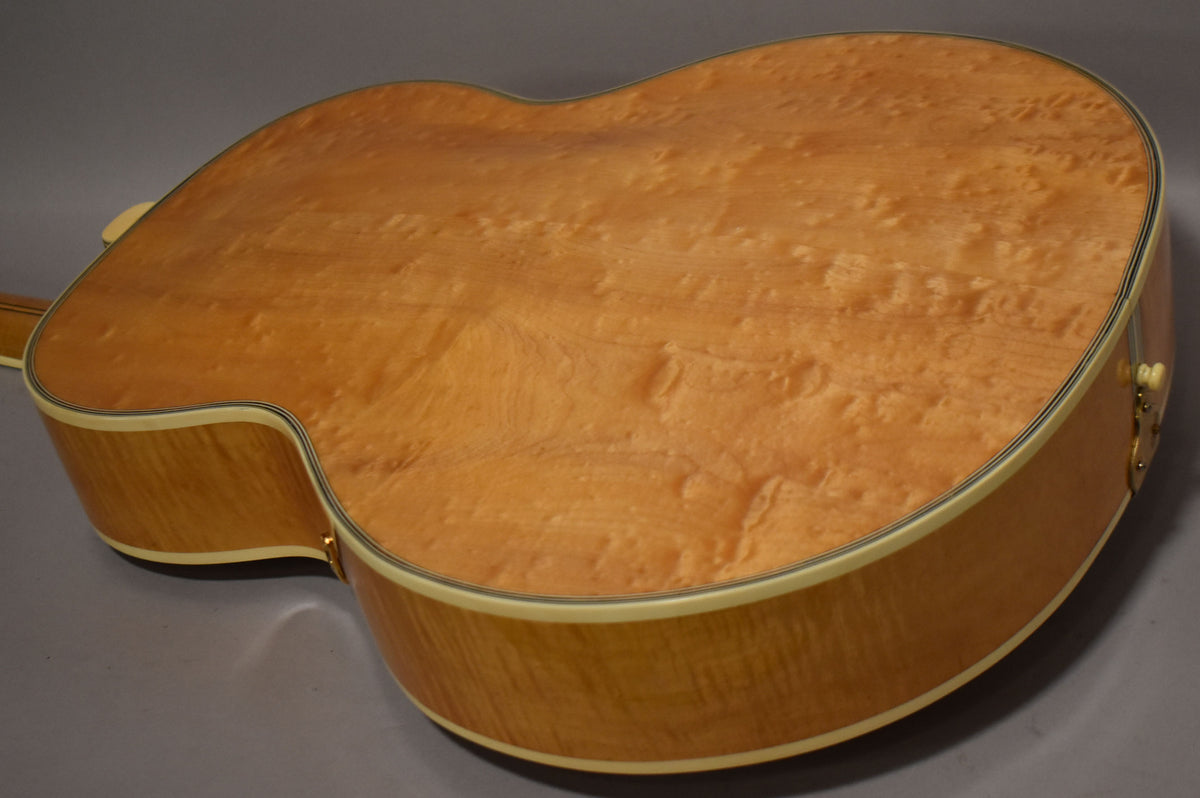 The back of the natural archtop acoustic guitar shows a curly maple finish, with light checking and a cream binding.