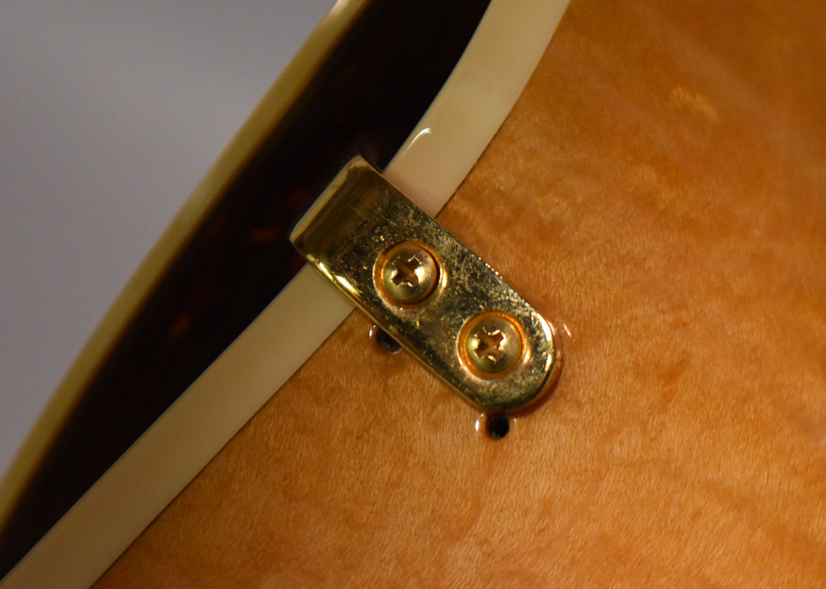 Close-up of the guitar's natural wood body, showing a gold-plated strap button with two screws and light finish checking.