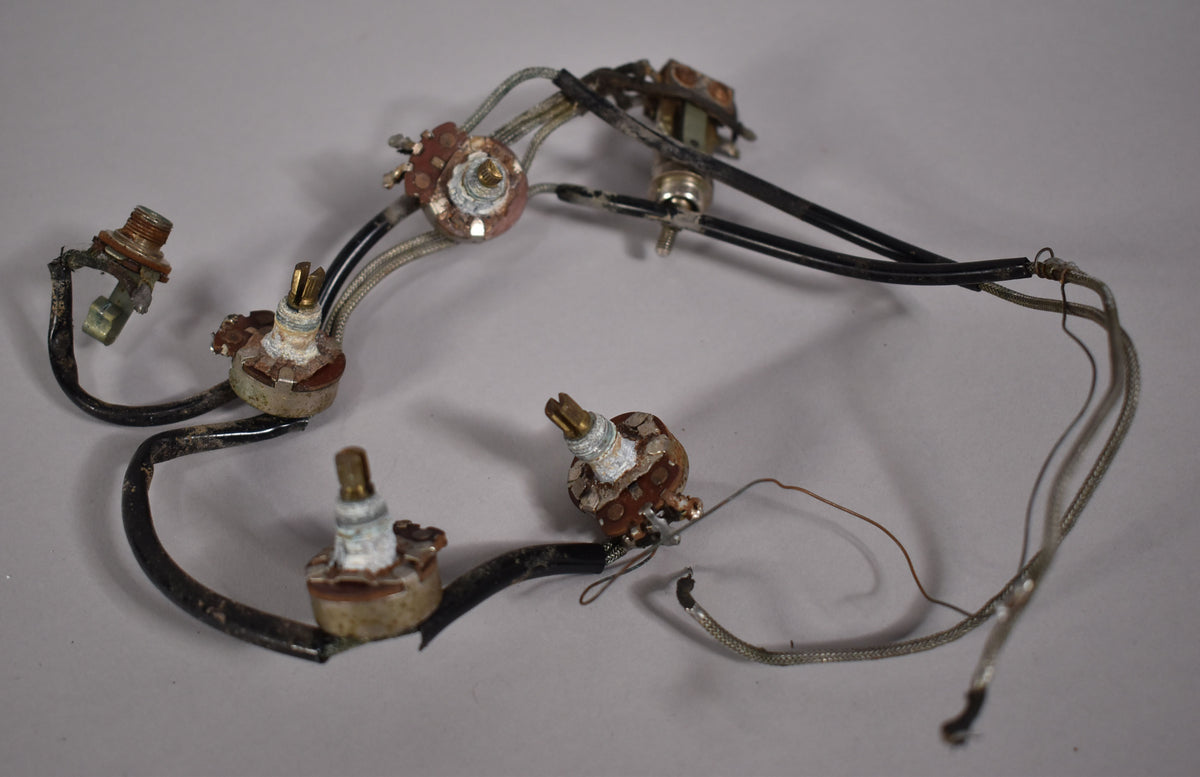 A close-up of the guitar's internal wiring harness, showing five tarnished potentiometers and frayed, discolored wires.