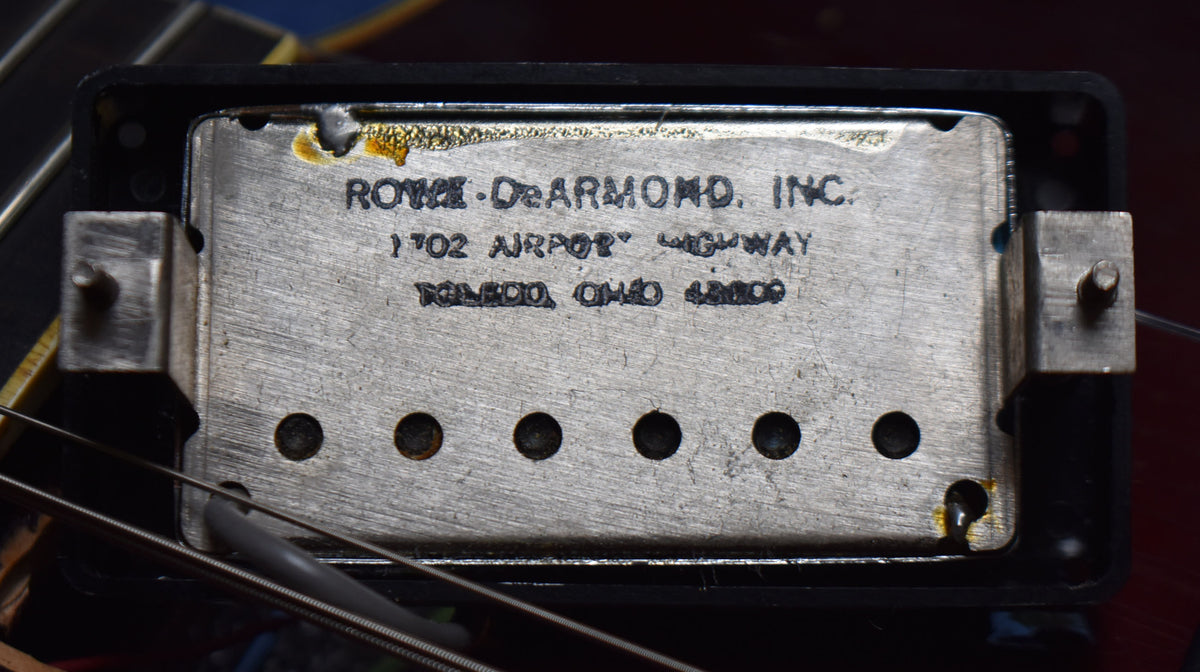 Close-up of a tarnished silver pickup with black lettering, six dark pole pieces, and visible corrosion at the top and bottom right.