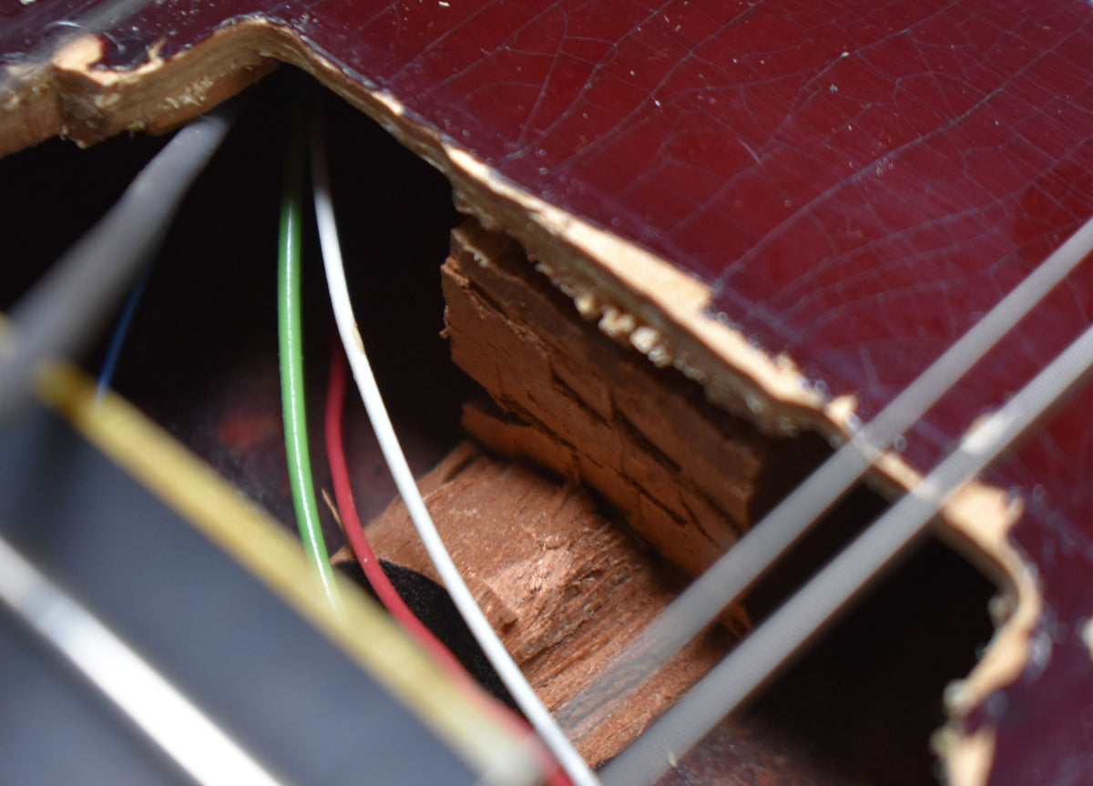 Close-up of the guitar's dark red body with heavy finish checking, revealing exposed wood and wiring inside a routed cavity.