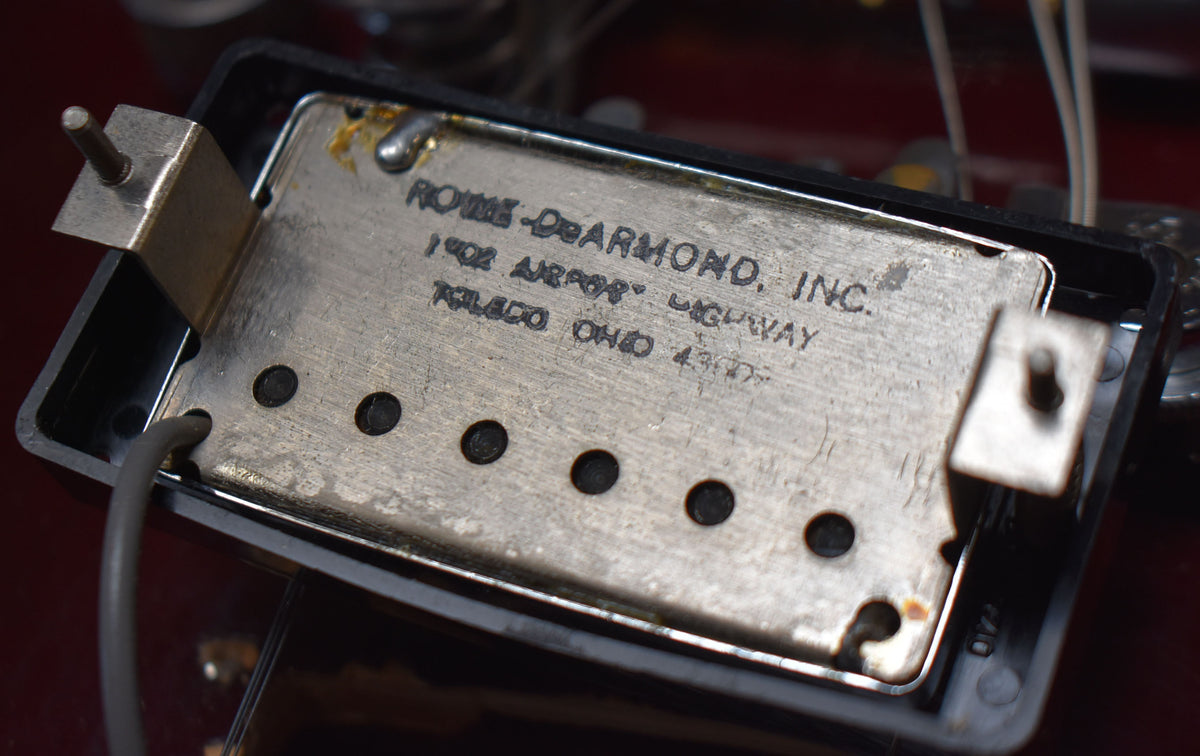 Close-up of the underside of a worn, tarnished silver pickup with black pole pieces, showing engraved text and mounting hardware.