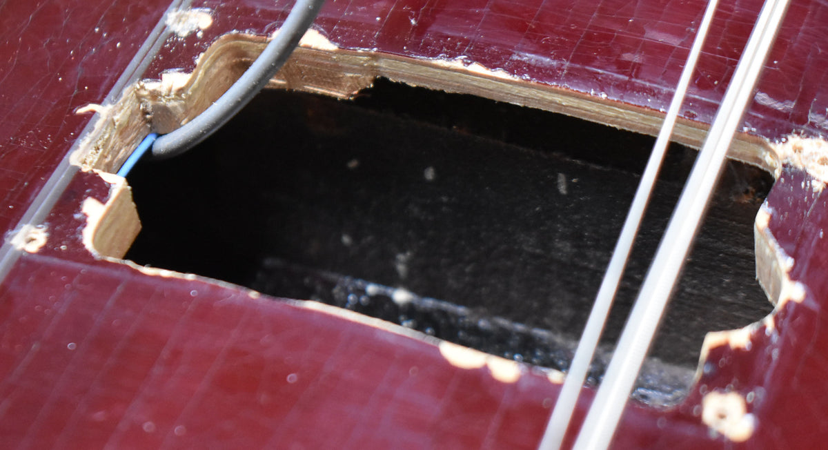 Close-up of a rectangular cavity in the dark red body, revealing rough wood edges, black interior, and two white wires.