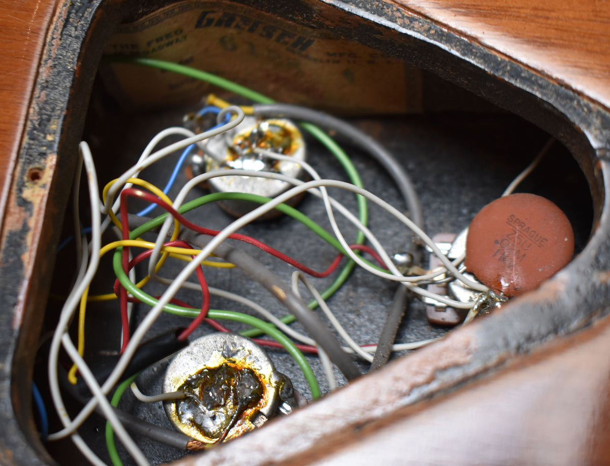 Close-up of the guitar's wiring cavity, showing colorful wires, two potentiometers, and a brown Sprague capacitor.
