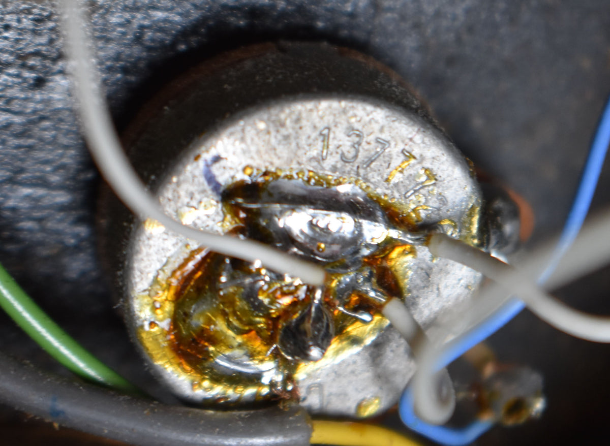 Close-up of a silver potentiometer with "137" stamped on top, surrounded by amber solder and connected by white, green, and blue wires.