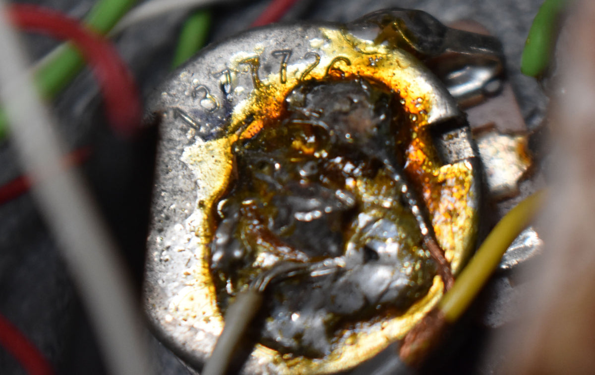 Extreme close-up of a silver-colored potentiometer with visible numbers "37726" and dark, amber-stained solder connections.