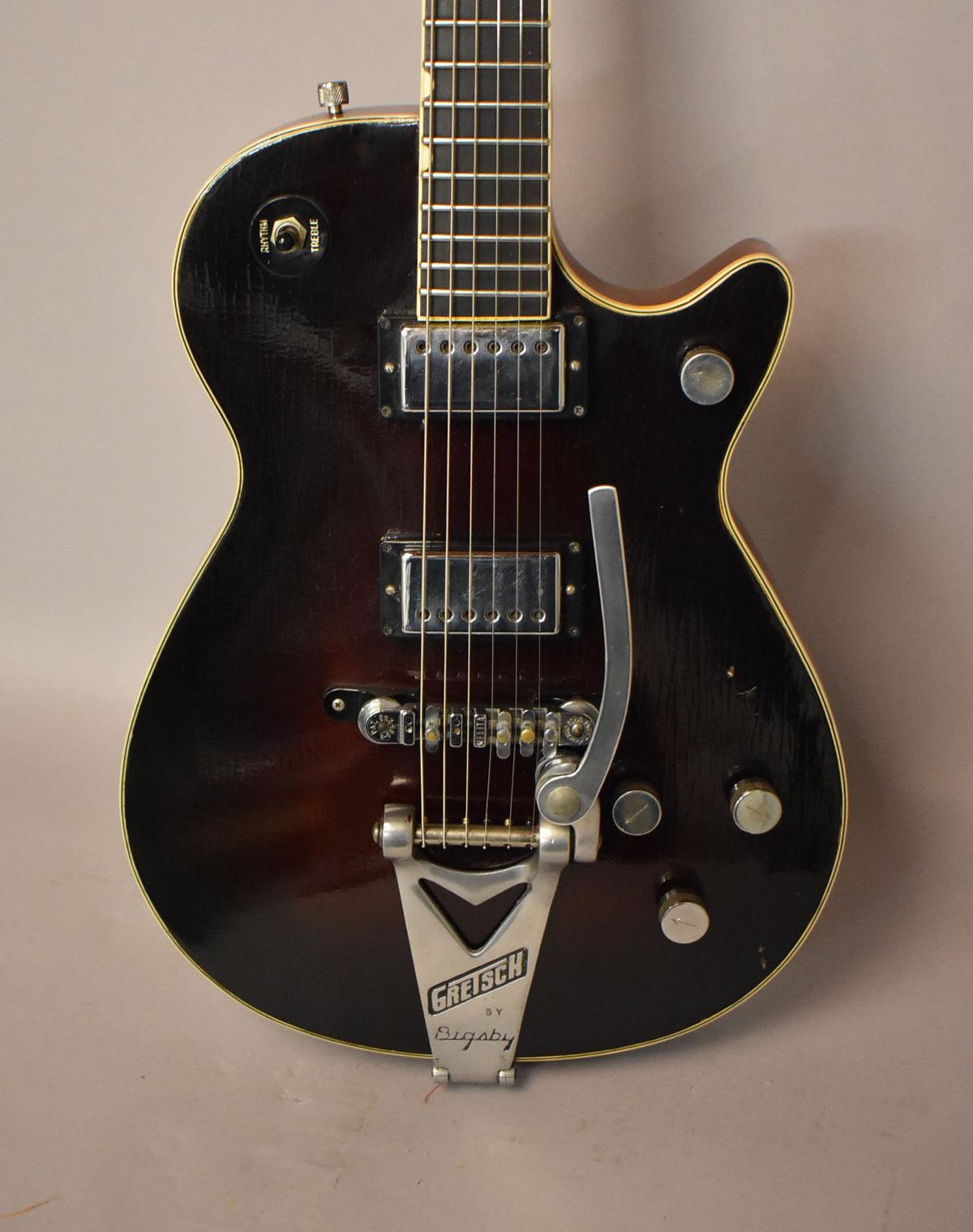 Full-frame view of a dark sunburst guitar with two chrome pickups, a Bigsby vibrato, and visible finish checking.