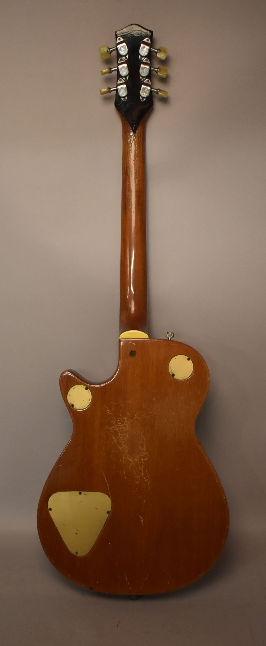 Full back view of a brown guitar with a glossy neck and a matte body showing heavy scratching, with three cream-colored control plates.