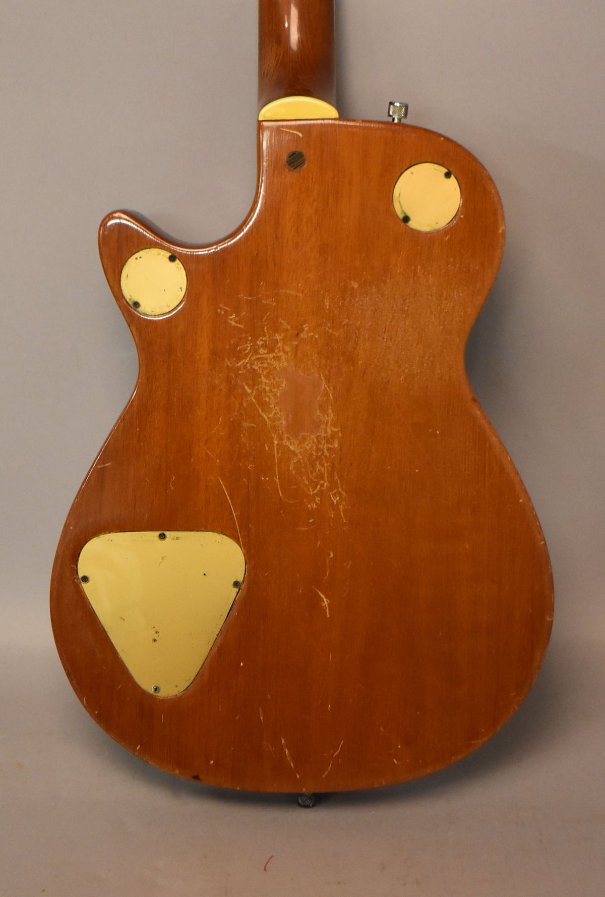 The back of a brown guitar body, showing three cream control cavity covers and heavy finish checking.