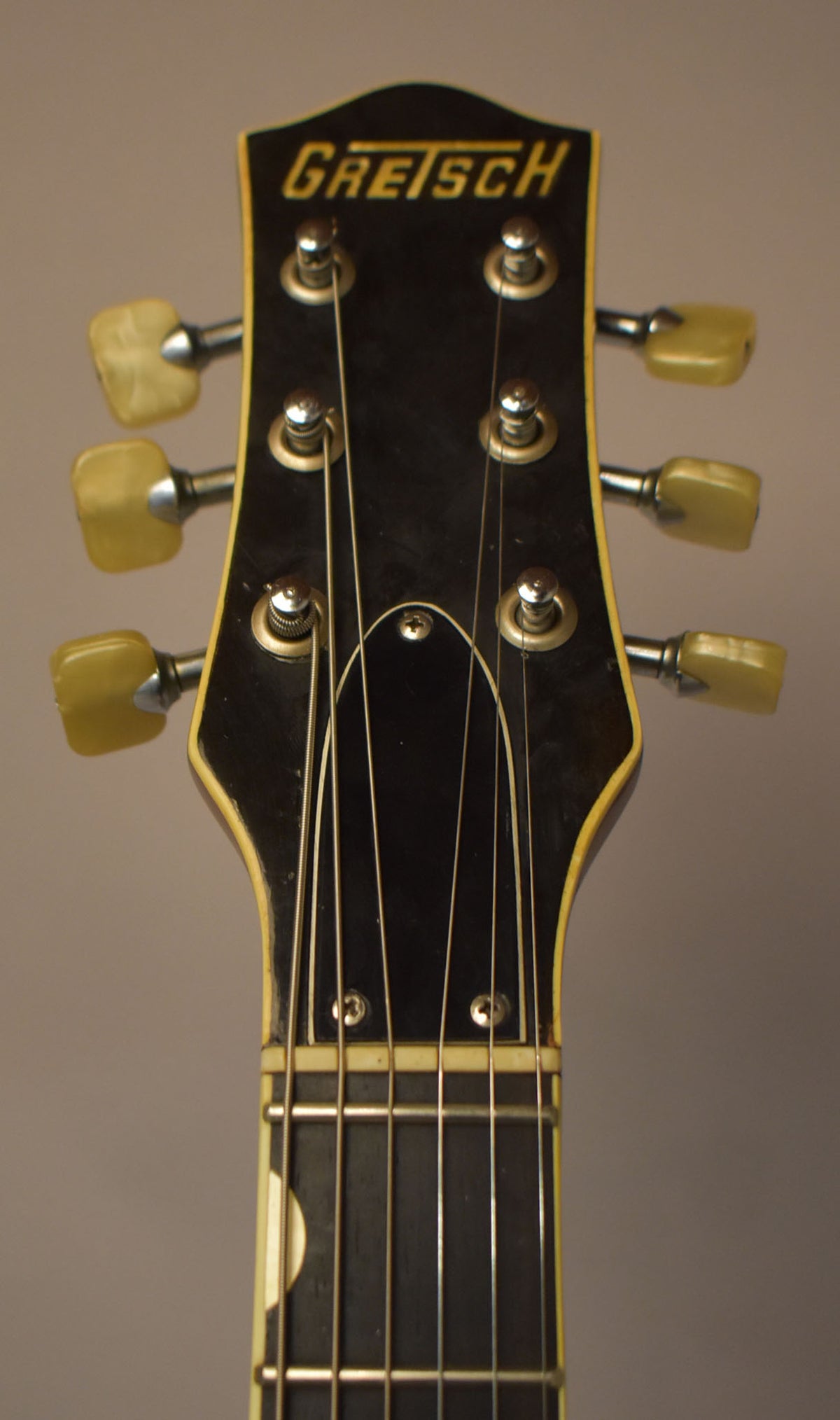 Close-up of the guitar's headstock, showing a black finish with gold lettering, six cream-colored tuning pegs, and some light wear.