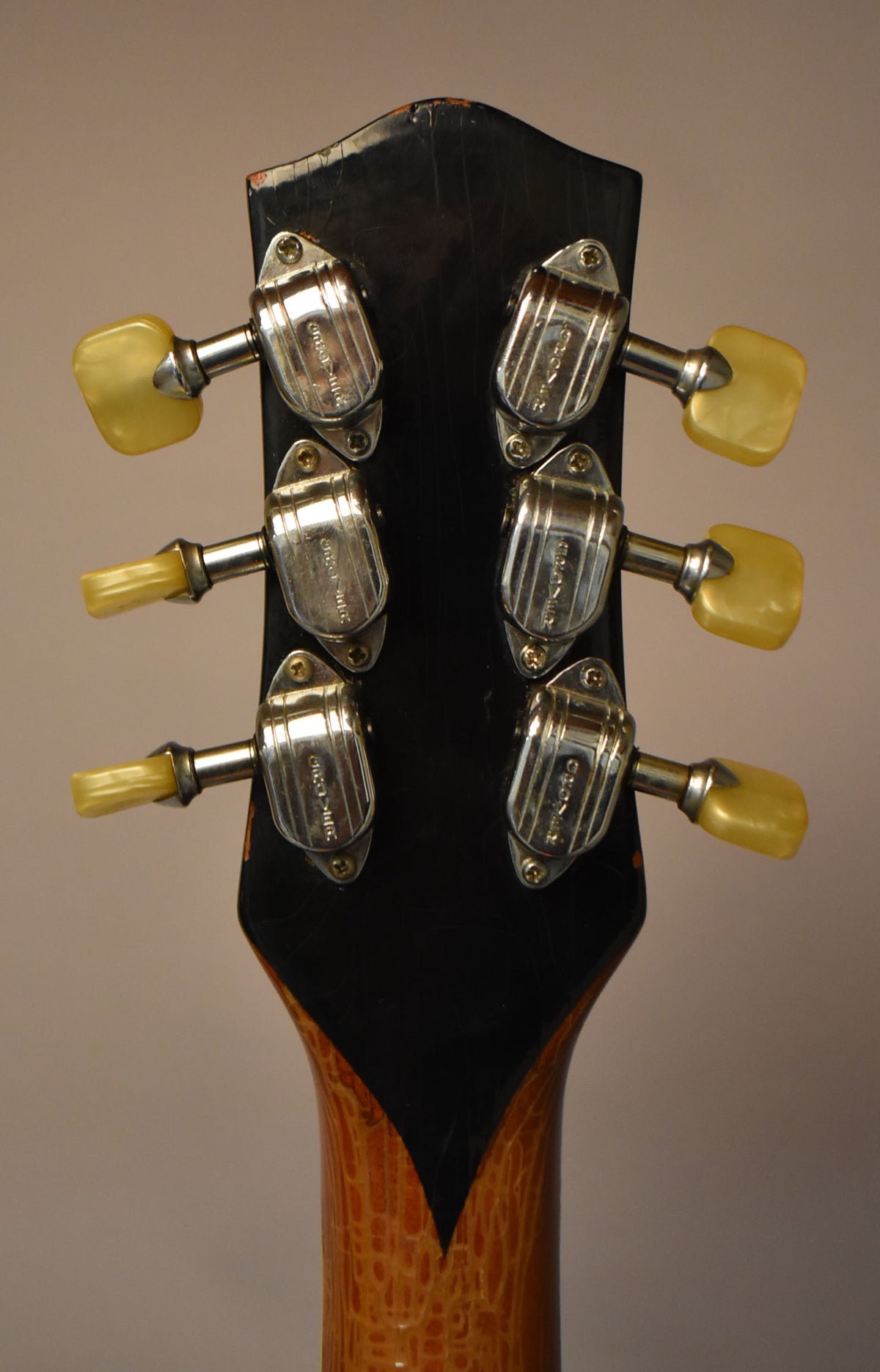 Rear view of the headstock, showing six chrome tuners with cream buttons, and heavy finish checking on the black and amber neck.