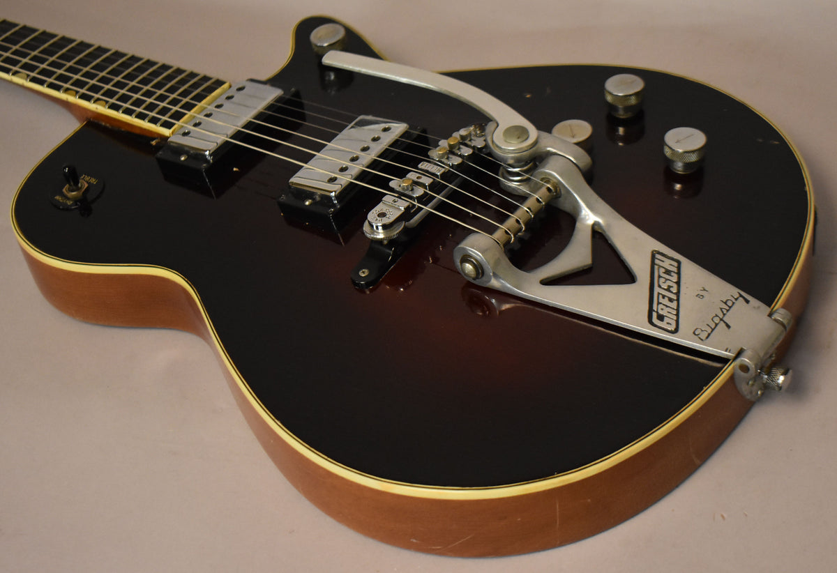 Close-up of a dark sunburst guitar body with a Bigsby vibrato, two chrome pickups, and four silver control knobs.