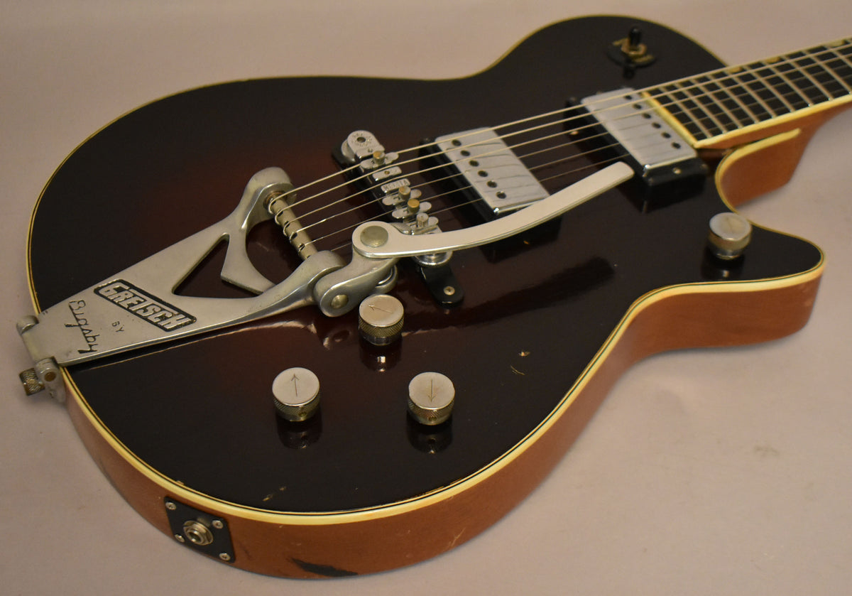 The dark brown sunburst guitar body, with cream binding, shows a Bigsby vibrato, two chrome pickups, and four silver control knobs.
