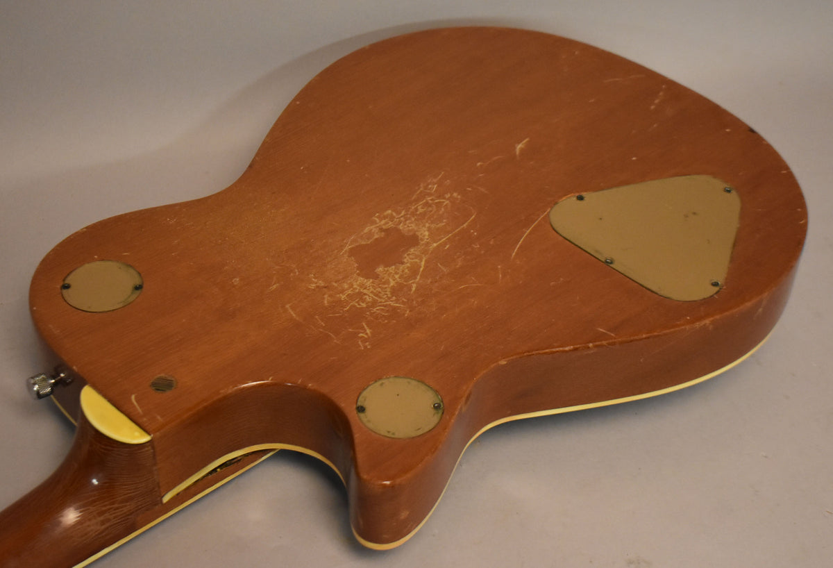 The guitar's dark brown back shows heavy finish wear, checking, and a large area of flaking, with three cream control plates.