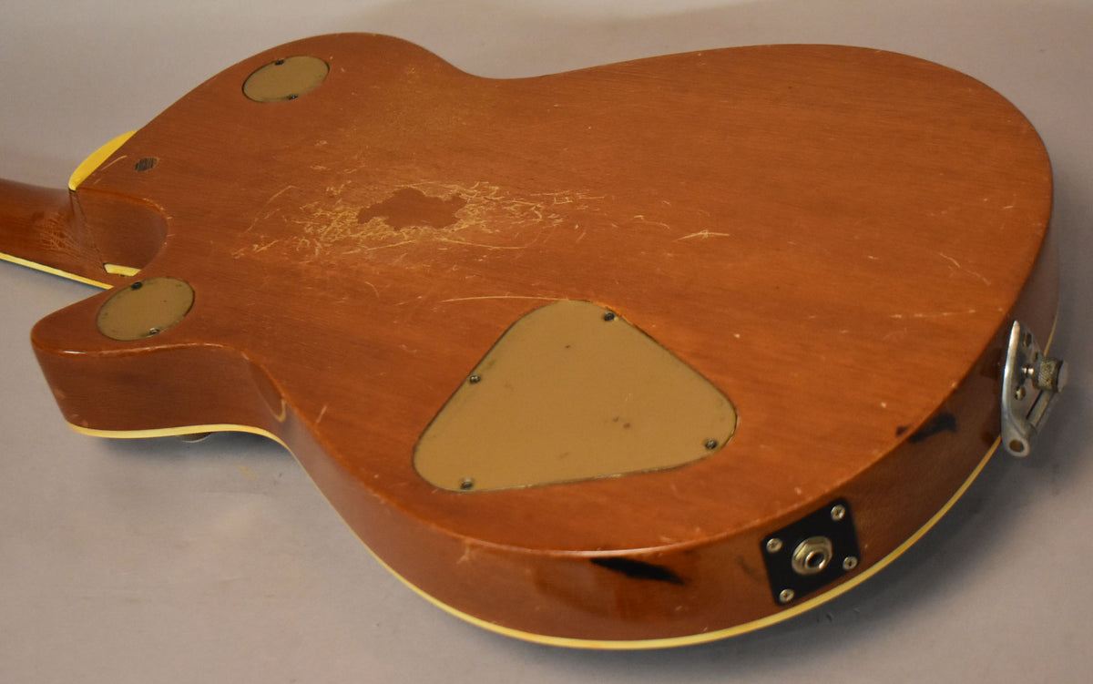 The guitar's refinished brown back shows extensive finish wear, checking, and scratches, with three tan control cavity covers.