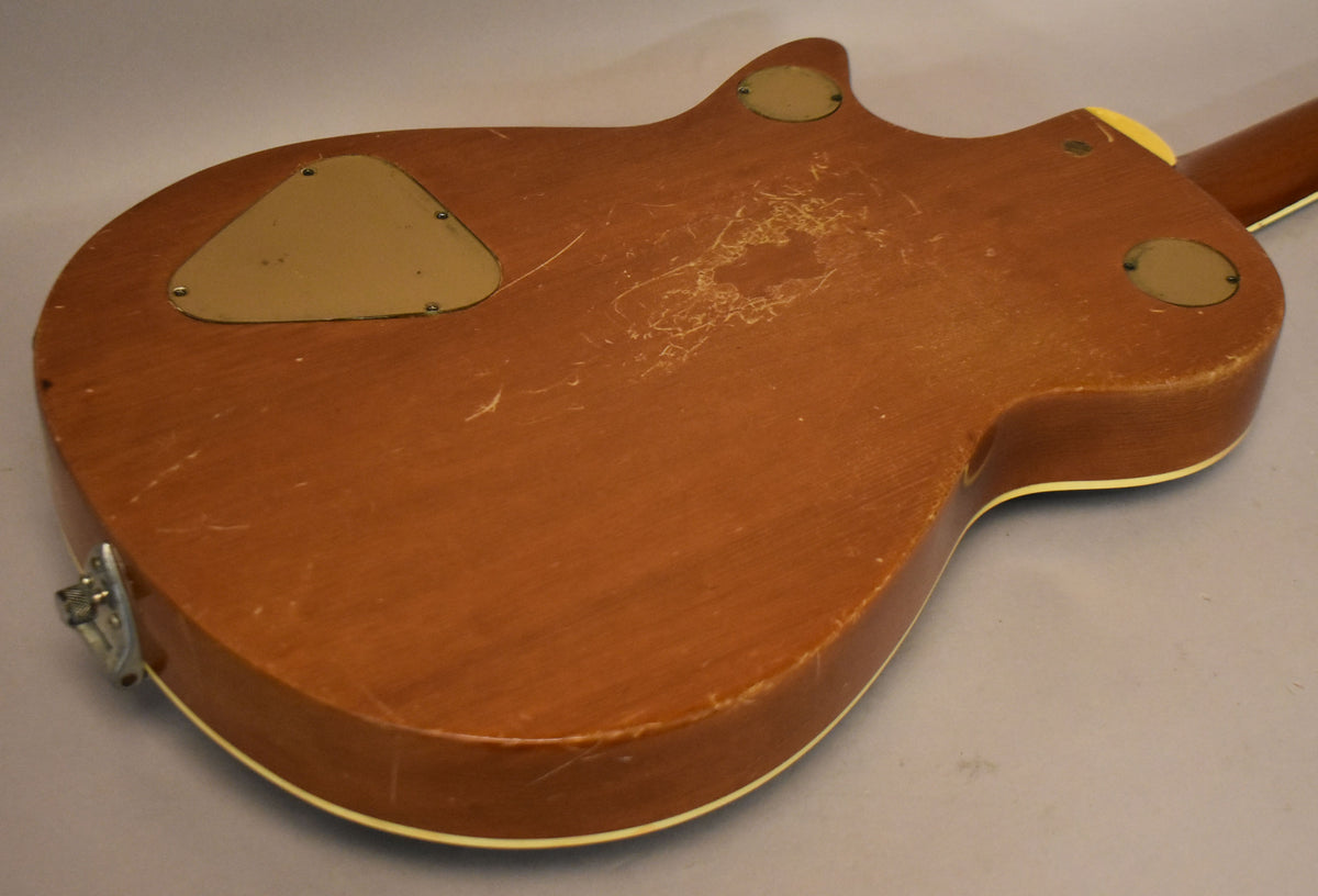 The guitar's dark brown back is heavily scratched and worn, with three tan control cavity covers and a chrome strap button.