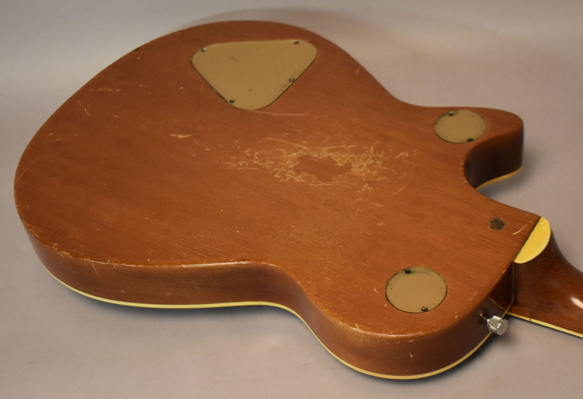 The guitar's dark brown back shows heavy wear, with large areas of finish loss and many scratches around three cream control plates.
