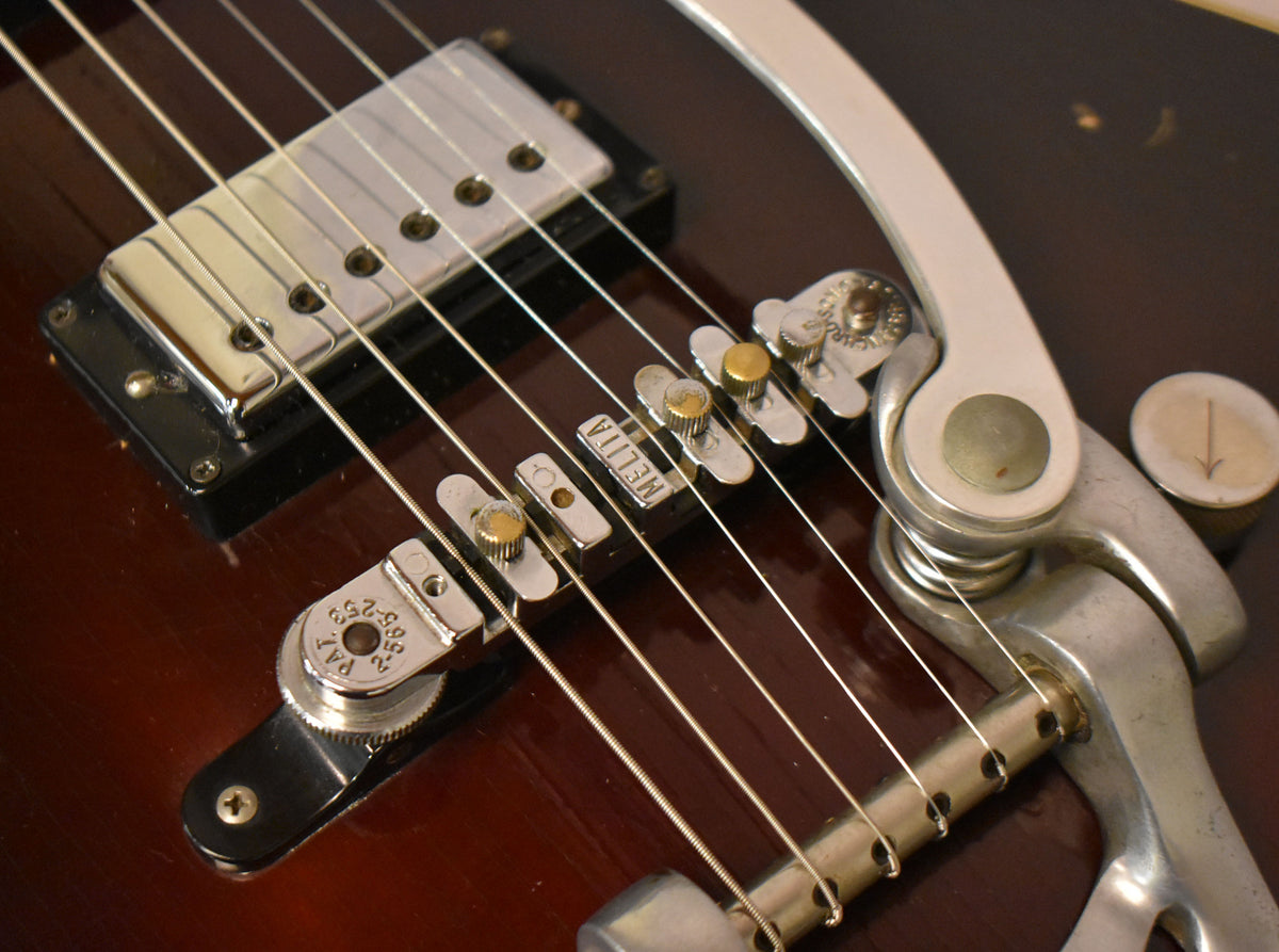 Close-up of the guitar's dark sunburst body, showing a chrome pickup, a Melita bridge, and a Bigsby vibrato tailpiece.